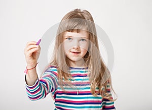 Pretty little girl holding a purple felt-tip pen and drawing something