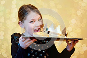 pretty little girl holding a tray with a galette des rois and a crown to celebrate the epiphany