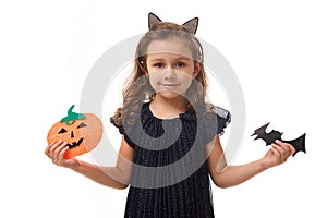 Pretty little girl with a hoop in the form of cat ears, dressed in a beautiful evening dress, holds felt-cut pumpkin and handmade