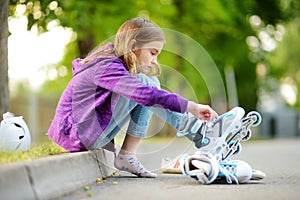 Pretty little girl learning to roller skate on summer day in a park. Child wearing safety helmet enjoying roller skating ride outd