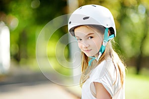 Pretty little girl learning to roller skate on summer day in a park. Child wearing safety helmet enjoying roller skating ride outd