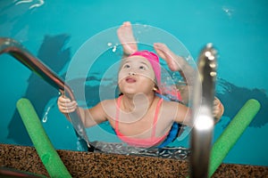 Pretty little girl learning to swim in the pool with swim coach trainer