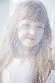 Pretty little girl looking through a curtain lace