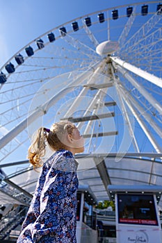 Pretty little girl looks at ferris wheel against a blue sky