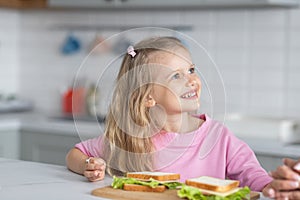 A pretty little girl mistress of the kitchen with a wide satisfied smile demonstrates the prepared sandwiches and looks