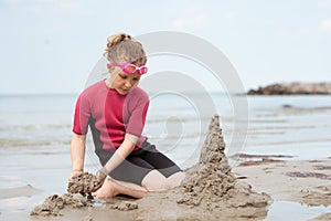 Pretty little girl in neoprene swimsuits playing with sand in sea
