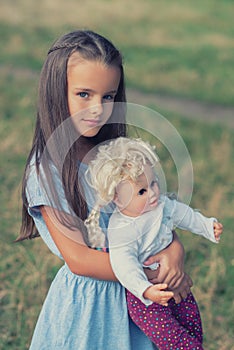 Pretty little girl posing  in blue dress with vintage doll, summer nature outdoor. Kid`s portrait.