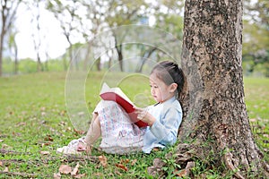 Pretty little girl reading a book sitting under a tree outdoor garden at summer day