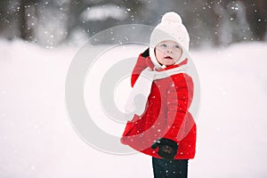 Pretty little girl in red coat in winter forest. cheerful little baby girl in gloves and white hat runs on snow white