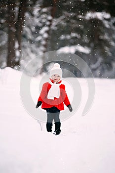 Pretty little girl in red coat in winter forest. cheerful little baby girl in gloves and white hat runs on snow white