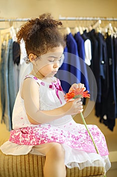 Pretty little girl with red flower sits at pouf in photo