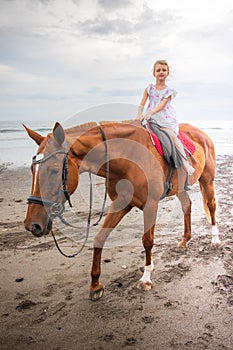Pretty little girl riding horse on the beach. Happy childhood. Sunset time by the sea. Outdoor activities. Vacation concept. Bali