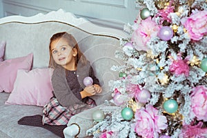 Pretty little girl sits on a sofa near Christmas tree and looks up