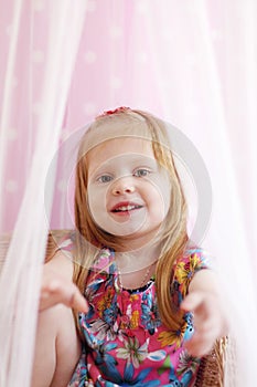 Pretty little girl sits among transparent curtains