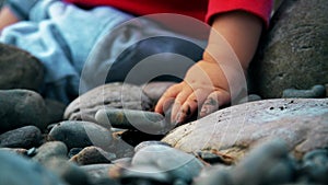 Pretty little girl is sitting on a bank of mountain river and playing with stones.