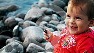 Pretty little girl is sitting on a bank of mountain river and playing with stones.