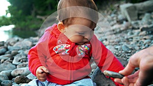 Pretty little girl is sitting on a bank of mountain river and playing with stones.