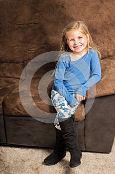 Pretty little girl sitting on a sofa with a big smile