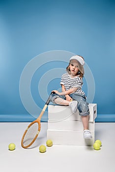pretty little girl sitting on white boxes and holding tennis raquet