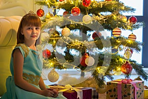 Pretty little girl smiling with present near the Christmas tree