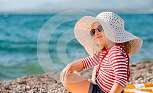 Pretty little girl in a striped dress, glasses and hat relaxing on the beach near sea, summer, vacation, travel -
