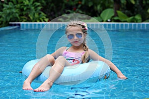 Pretty little girl swimming in outdoor pool and have a fun with inflatable circle