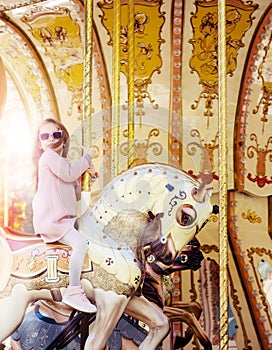 Pretty little girl, wearin sunglusses, riding the horse of merry-go-round.