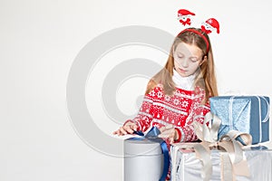 Pretty little girl wearing Christmas headband sitting isolated on white background,holding stack of present boxes