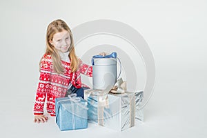 Pretty little girl wearing Christmas sweater sitting isolated on white background, holding stack of present boxes.Merry