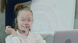 Pretty little girl wearing headset using laptop and talking to her colleague