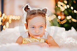 a pretty little girl in a white dress with a gift in gold wrapping paper.