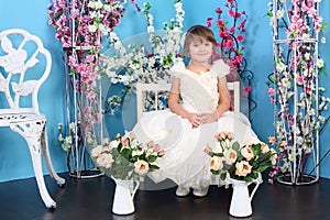 Pretty little girl in white dress sits on chair in photo