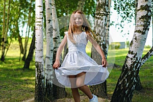 Pretty little girl in white dress whirls and dances among the trees