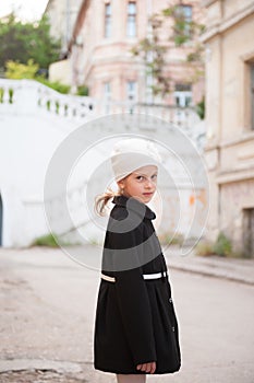 Pretty little girl in white hat and black retro style coat on old town street