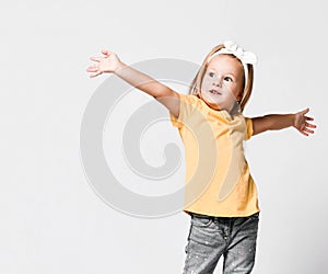 Pretty little kid baby girl in yellow t-shirt is singing with her hands up spread, dancing, playing role, makes show