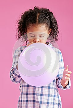 A pretty little mixed race girl with curly hair blowing a balloon against a pink copyspace background in a studio