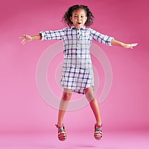 A pretty little mixed race girl with curly hair celebrating and dancing against a pink copyspace background in a studio