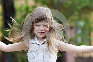 Pretty little preschool girl in sleeveless white dress with beautiful long blond hair blown by wind, funny toothless smile and spr