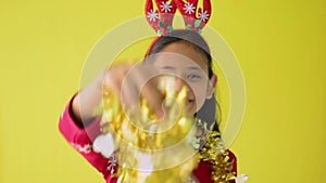 Pretty long hair girl in red sweater wearing reindeer antlers headband is dancing with golden Christmas garland happily.