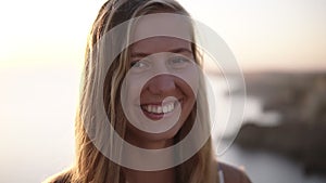 Pretty long haired blonde woman looking straight to the camera and smiling, a little shy. Beautiful nature blurred