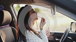 Pretty long-haired girl applying lipstick at car front mirror