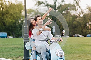 Pretty long-haired young woman enjoying trip on scooter with boyfriend. Blissful loving couple riding around park and