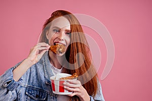 Pretty long redhead ginger girl eating fries chicken in studio pink background