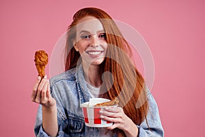 Pretty long redhead ginger girl eating fries chicken in studio pink background