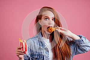 Pretty long redhead ginger girl eating fries chicken in studio pink background