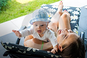 Pretty loving mom trying to soothe scarred crying baby in mother`s arms outdoor at sun deck chair