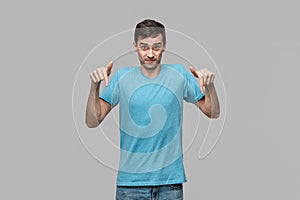 Pretty man in a blue tee pointing with a finger at the copy space isolater over grey background.