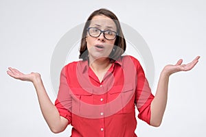 Pretty mature caucasian woman in red shirt and glasses shrugs shoulders with open palms