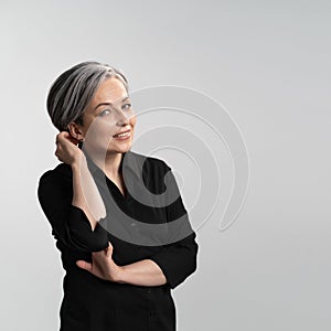 Pretty mature woman corrects her hairstyle. Caucasian female model wearing black shirt looks at camera with beautiful