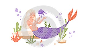 Pretty mermaid with long blonde hair and fish tail playing with jellyfish at sea bed. Cute underwater fairy princess